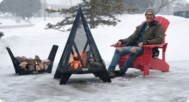Man enjoying a winter fire in a Pyramid Fire pit from his Adirondack chair