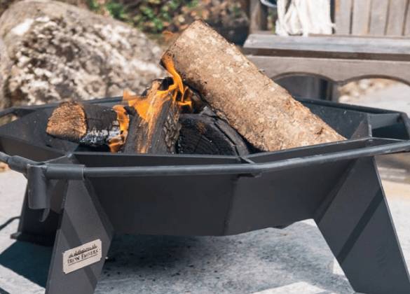 Small steel fire pit on a stone patio burning large logs