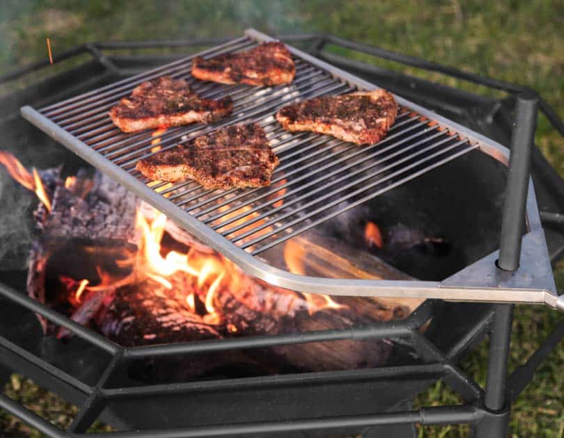 Stainless adjustable bbq grill with steaks on the fire