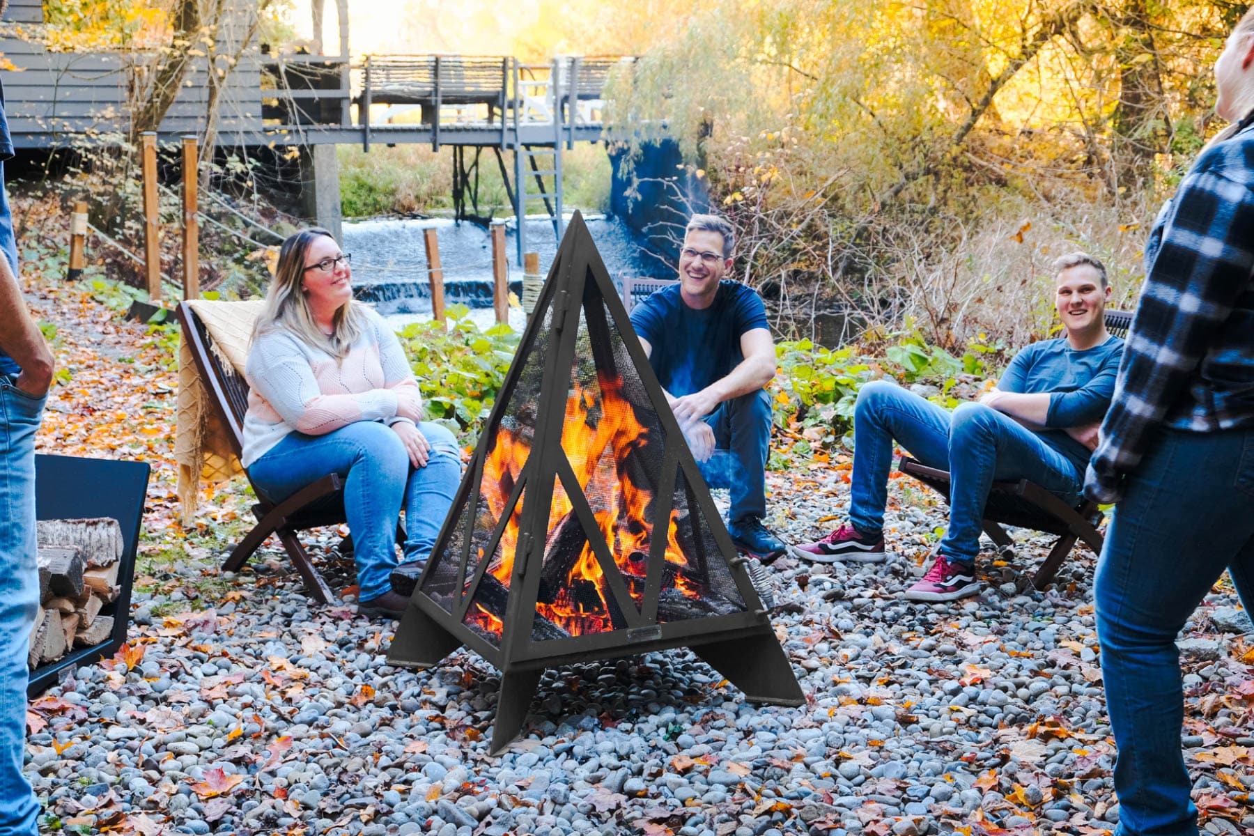 People sitting near pyramid fire pit fireplace near a creek