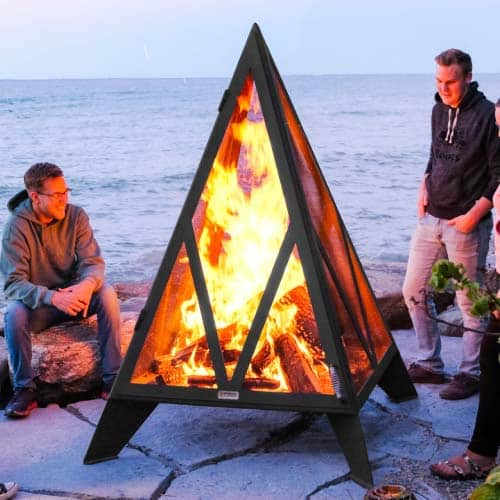 Large pyramid fire pit with fire burning near a lake at sunset